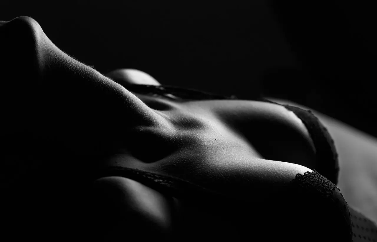 Close-up black and white boudoir photograph of a woman’s torso in lingerie, highlighting curves and shadows in soft artistic lighting.