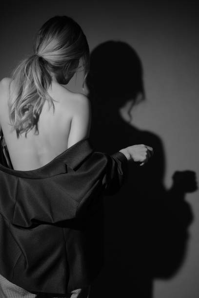 Blonde woman seen from behind, slipping off a jacket, casting a sensual shadow on the wall.